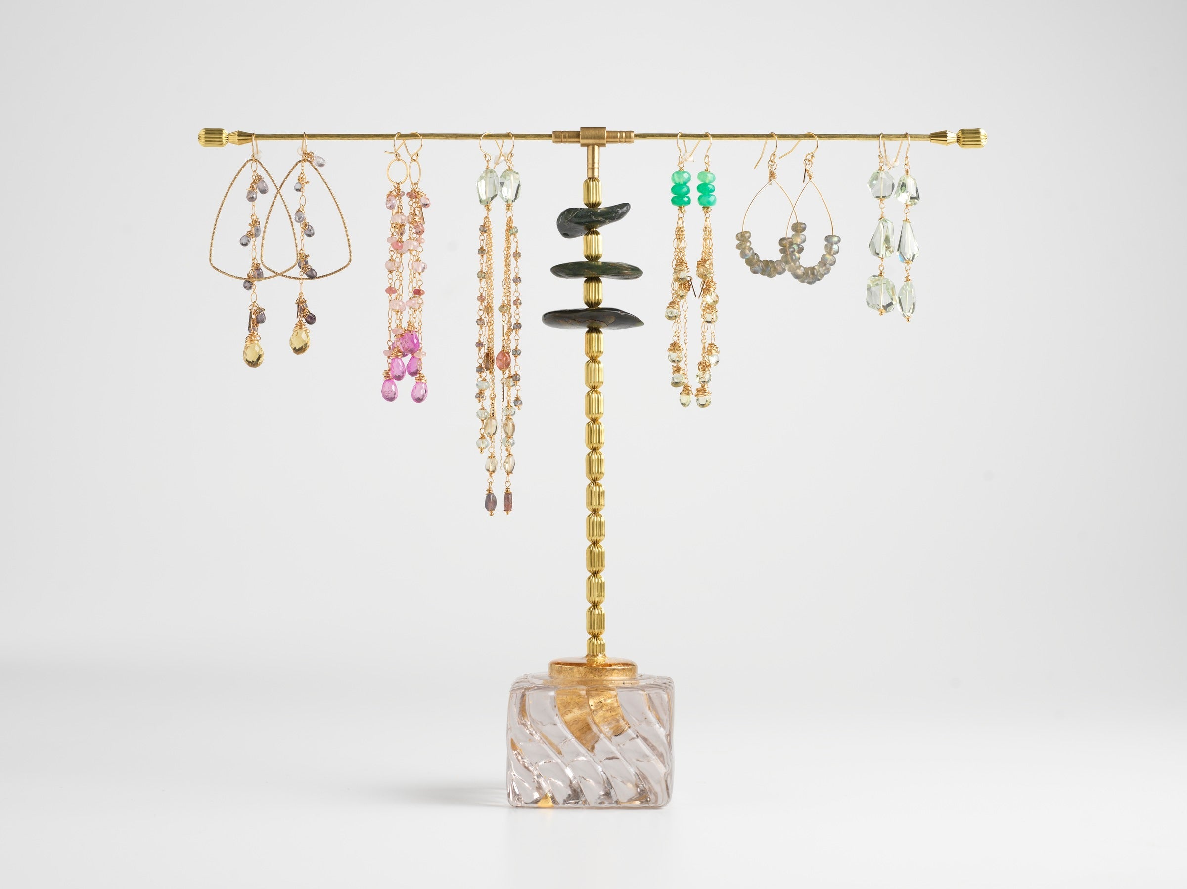 Six pairs of gemstone earrings hanging from a brass and jade display stand